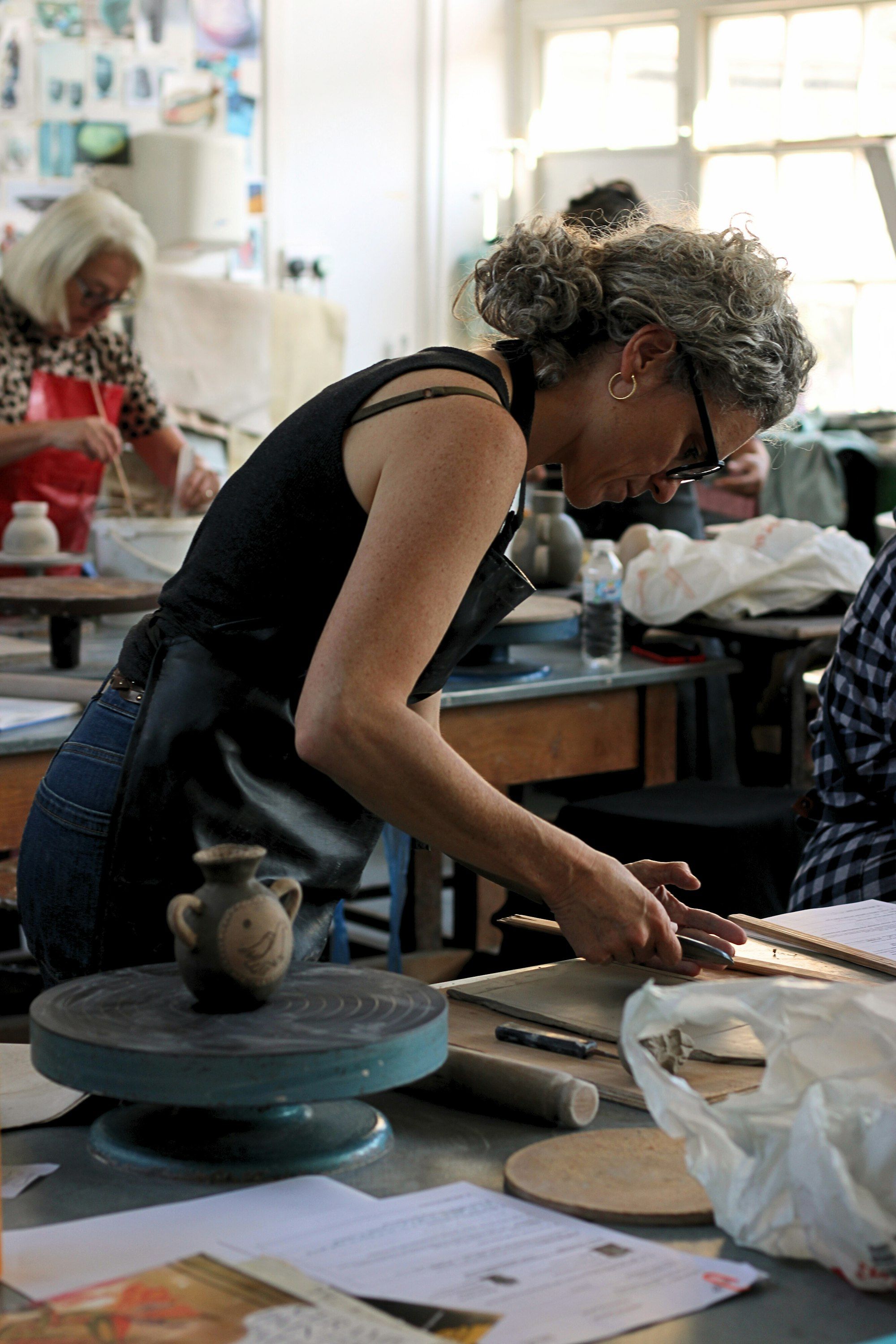 A woman working with clay at a table in a sunlit art studio