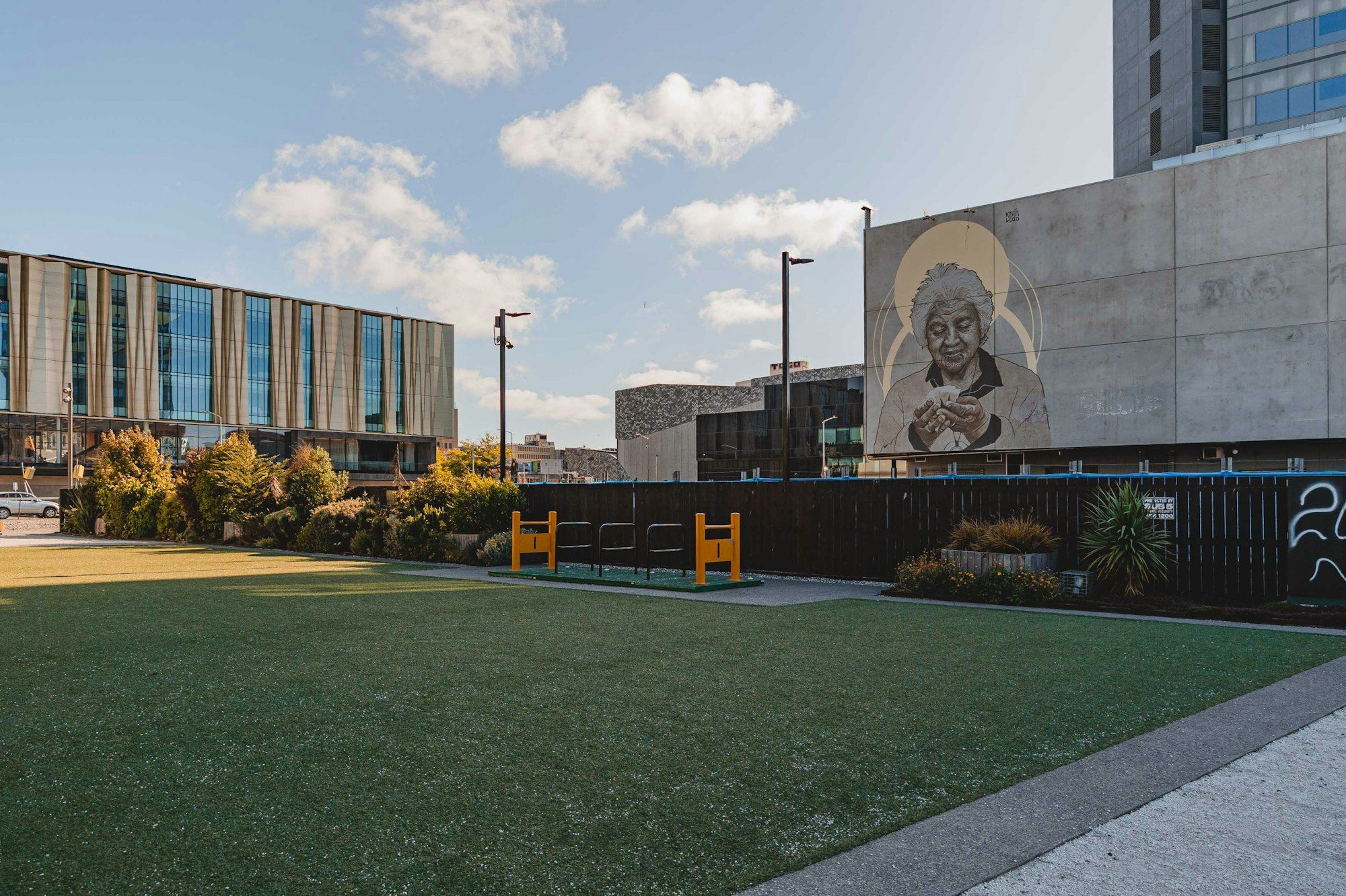 A modern grey building with a mural and a wide green lawn in central Christchurch